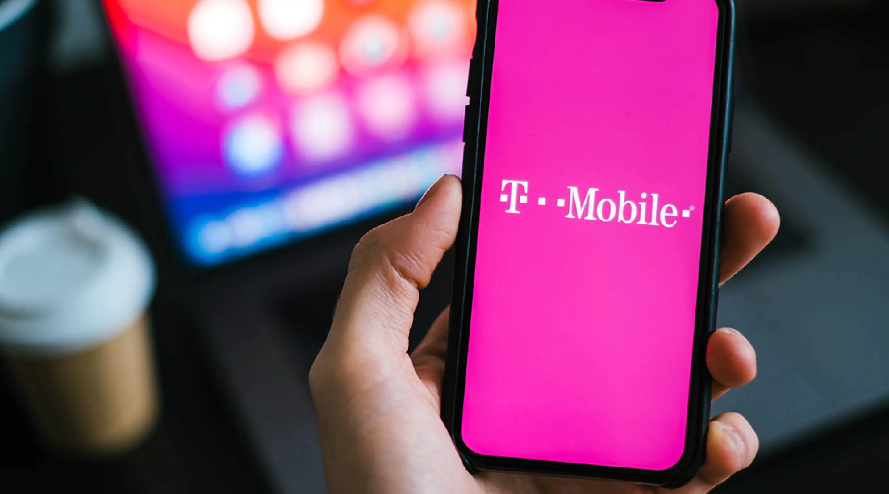 Closeup of a hand holding a mobile phone with the T-Mobile Logo on the screen